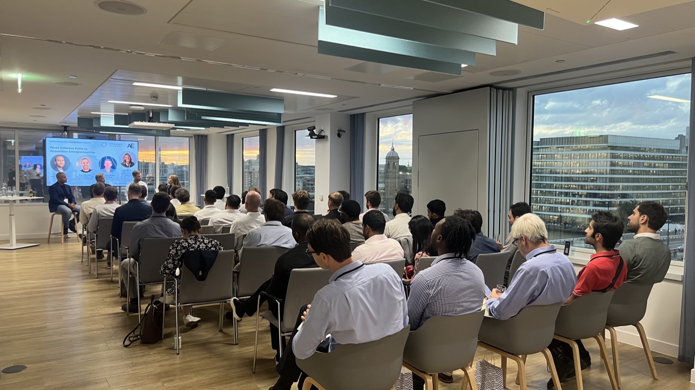 Rows of attendees facing a four-person panel in a glass-walled room at Howard Kennedy, with the London skyline at sunset through the windows.