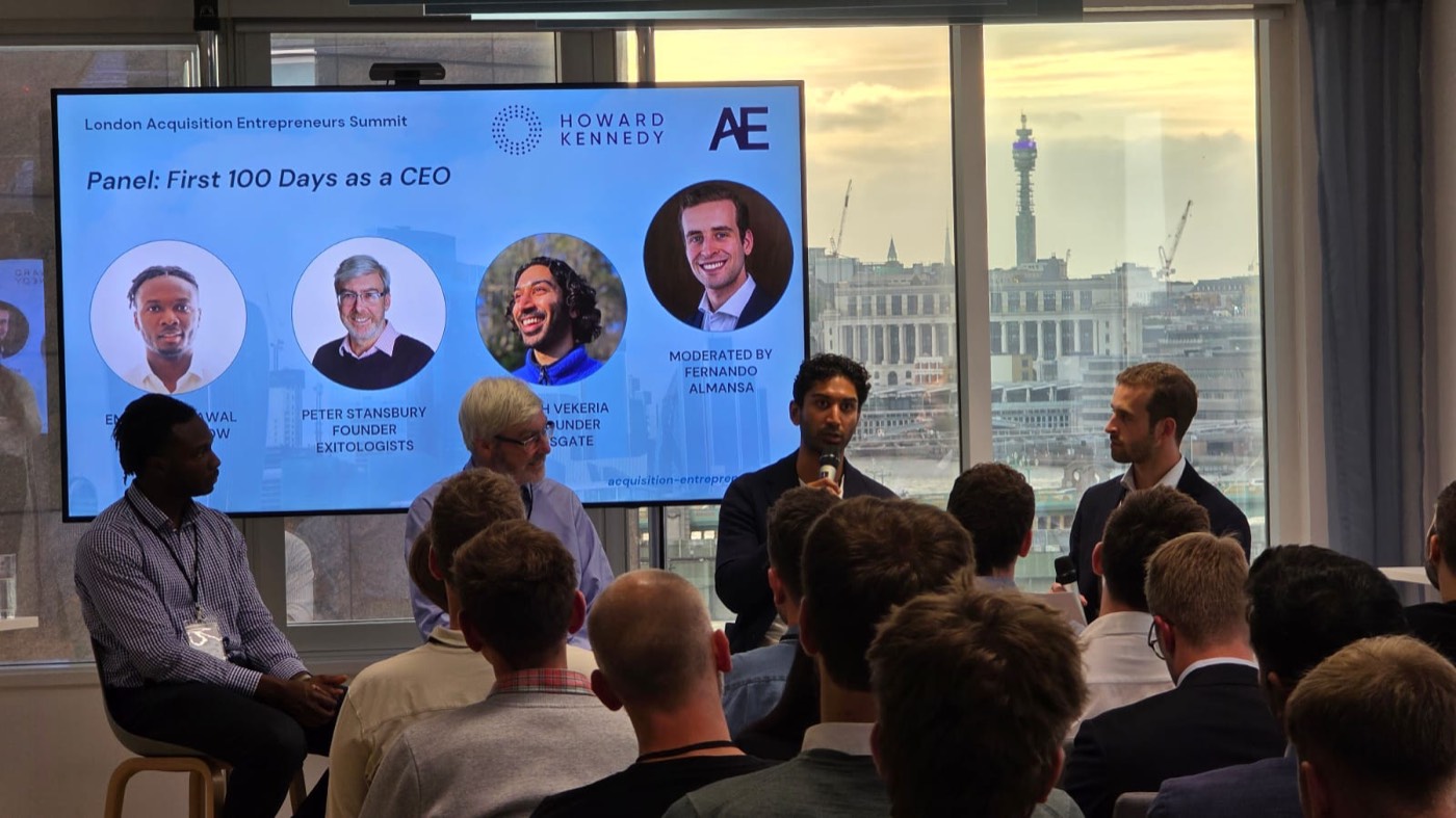 Four panellists seated in front of a screen titled 'Panel: First 100 Days as a CEO', one speaking into a microphone, with the BT Tower visible through the window.